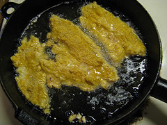 ajun tilapia fillets frying in a cast iron skillet with oil