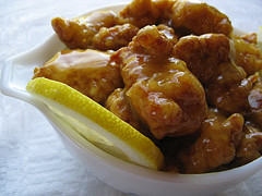 Chinese lemon chicken served in a white bowl with lemon slices and glossy lemon sauce on crispy battered chicken