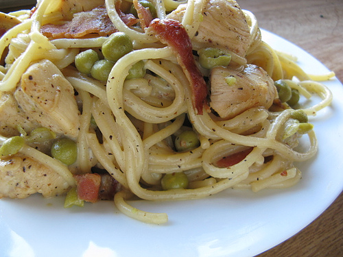 Plate of chicken carbonara pasta with spaghetti, peas, chicken pieces, and bacon