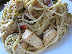 Plate of chicken carbonara pasta with spaghetti, peas, chicken pieces, and bacon