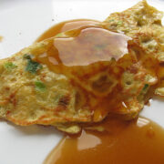 Egg foo yung patty topped with sauce on a white plate.