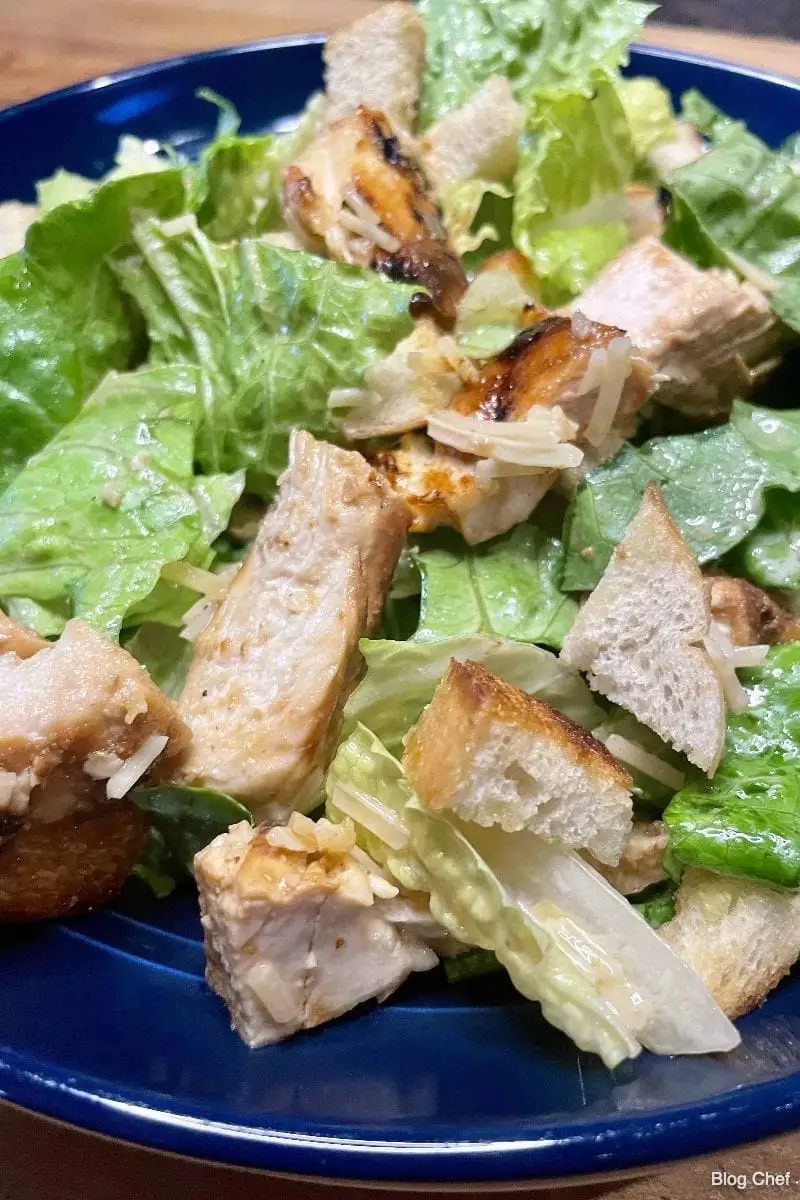 Top view of prepared chicken Caesar salad on blue plate.