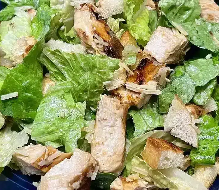Top view of prepared chicken Caesar salad on blue plate.