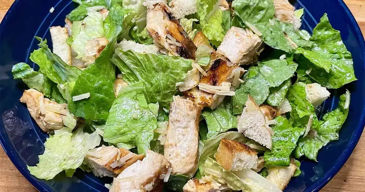 Top view of prepared chicken Caesar salad on blue plate.