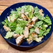 Top view of prepared chicken Caesar salad on blue plate.