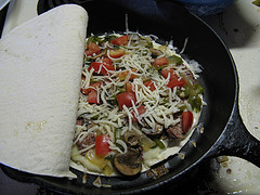 Tortilla in skillet topped with steak strips and melted cheese