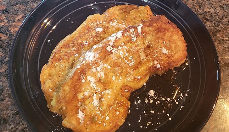 French toast on plate with powdered sugar and syrup.