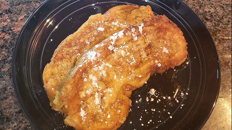 French toast on plate with powdered sugar and syrup.