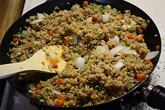 Shrimp fried rice cooking in a wok with peas, carrots, onions, and a wooden spatula