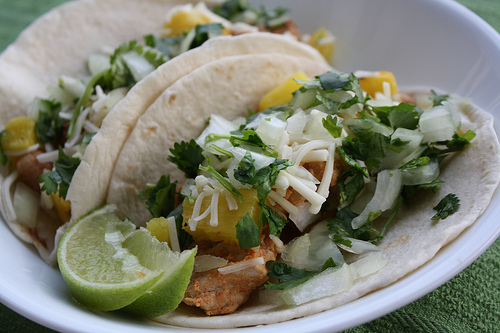 Taco filled with grilled pork, pineapple, cheese, onion, and cilantro with lime wedge
