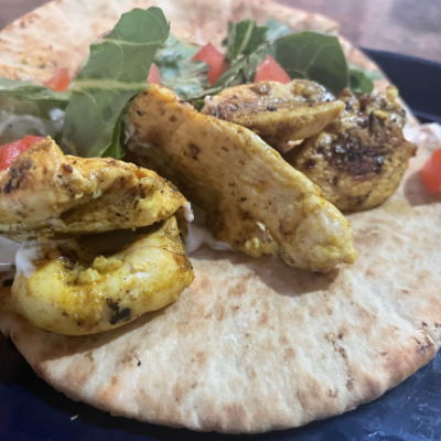 Prepared chicken shawarma on pita with lettuce, tomato, and sauce.