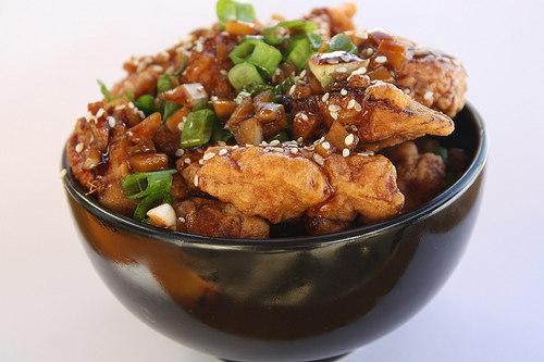 Garlic ginger chicken topped with green onions in a black bowl.
