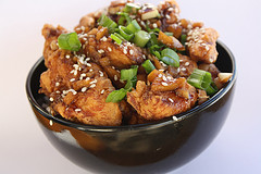 Garlic ginger chicken topped with green onions in a black bowl.
