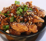 Garlic ginger chicken topped with green onions in a black bowl.
