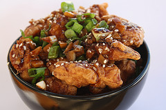 Garlic ginger chicken topped with green onions in a black bowl.