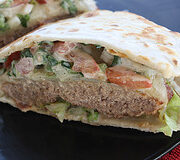 Quesadilla burger on a black plate with melted cheese and fresh toppings