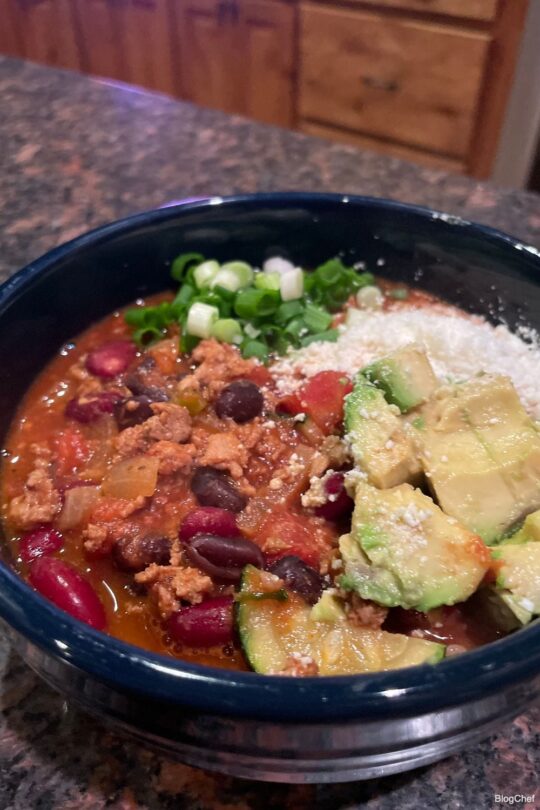 Prepared turkey chili with green onions, cotija cheese, and avocado.