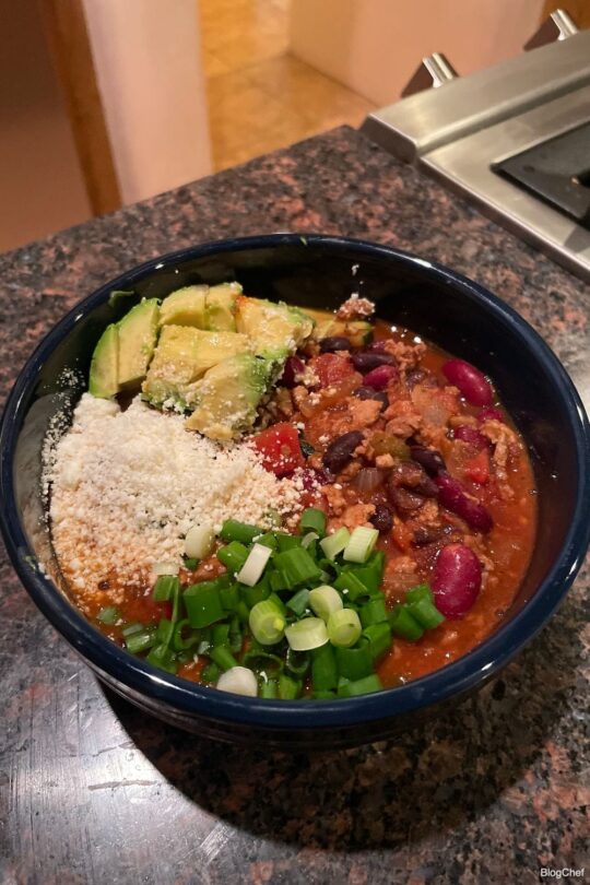 Prepared turkey chili with green onions, cotija cheese, and avocado.