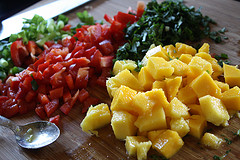 Diced mango, red bell pepper, and fresh herbs on a cutting board ready for salsa