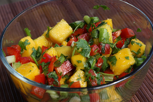 Glass bowl of mango salsa with bright mango chunks, peppers, and herbs