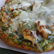 Baked chicken pesto pizza topped with melted mozzarella cheese on a plate