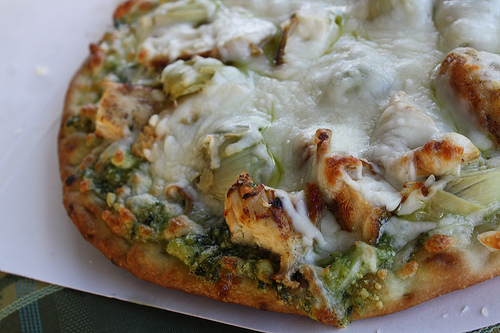 Baked chicken pesto pizza topped with melted mozzarella cheese on a plate