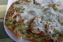Baked chicken pesto pizza topped with melted mozzarella cheese on a plate
