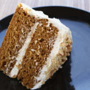 Slice of spice cake with cream cheese frosting on a black plate.
