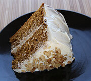 Slice of spice cake with cream cheese frosting on a black plate.