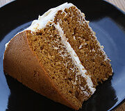 Slice of spice cake with cream cheese frosting on a black plate.