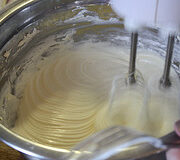 Cream cheese frosting being whipped with an electric mixer.