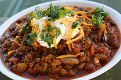 Bowl of pumpkin chili topped with shredded cheese and fresh herbs