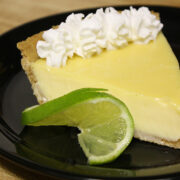 Slice of key lime pie with whipped cream and lime wedge on black plate