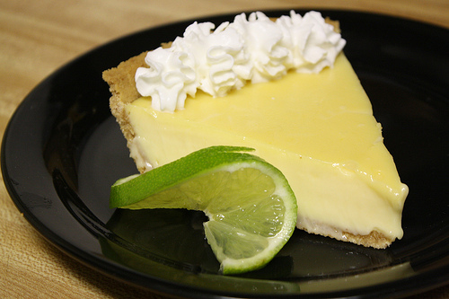Slice of key lime pie with whipped cream and lime wedge on black plate