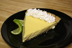 Slice of key lime pie with whipped cream and lime wedge on black plate