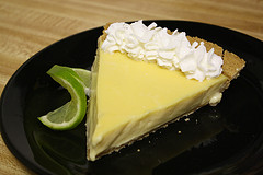 Slice of key lime pie with whipped cream and lime wedge on black plate