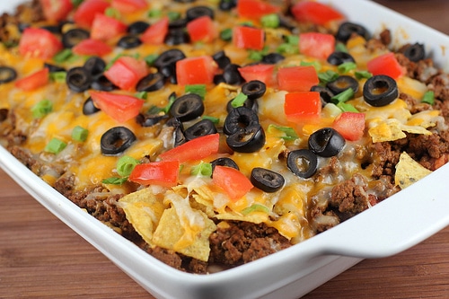 Mexican casserole topped with melted cheese, olives, tomatoes, and green onions