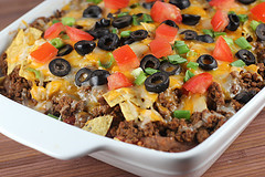 Mexican casserole topped with melted cheese, olives, tomatoes, and green onions