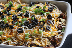 Mexican casserole with beef, melted cheese, black olives, and tomatoes in white baking dish