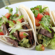Grilled steak tacos filled with lettuce, tomato, onion, and cheese on a white plate