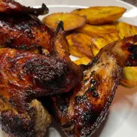 Close up view of jerk chicken on plate with plantains.