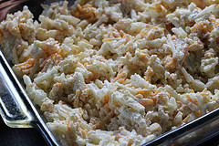 Shredded hashbrowns mixed with cheese and sauce in a glass baking dish