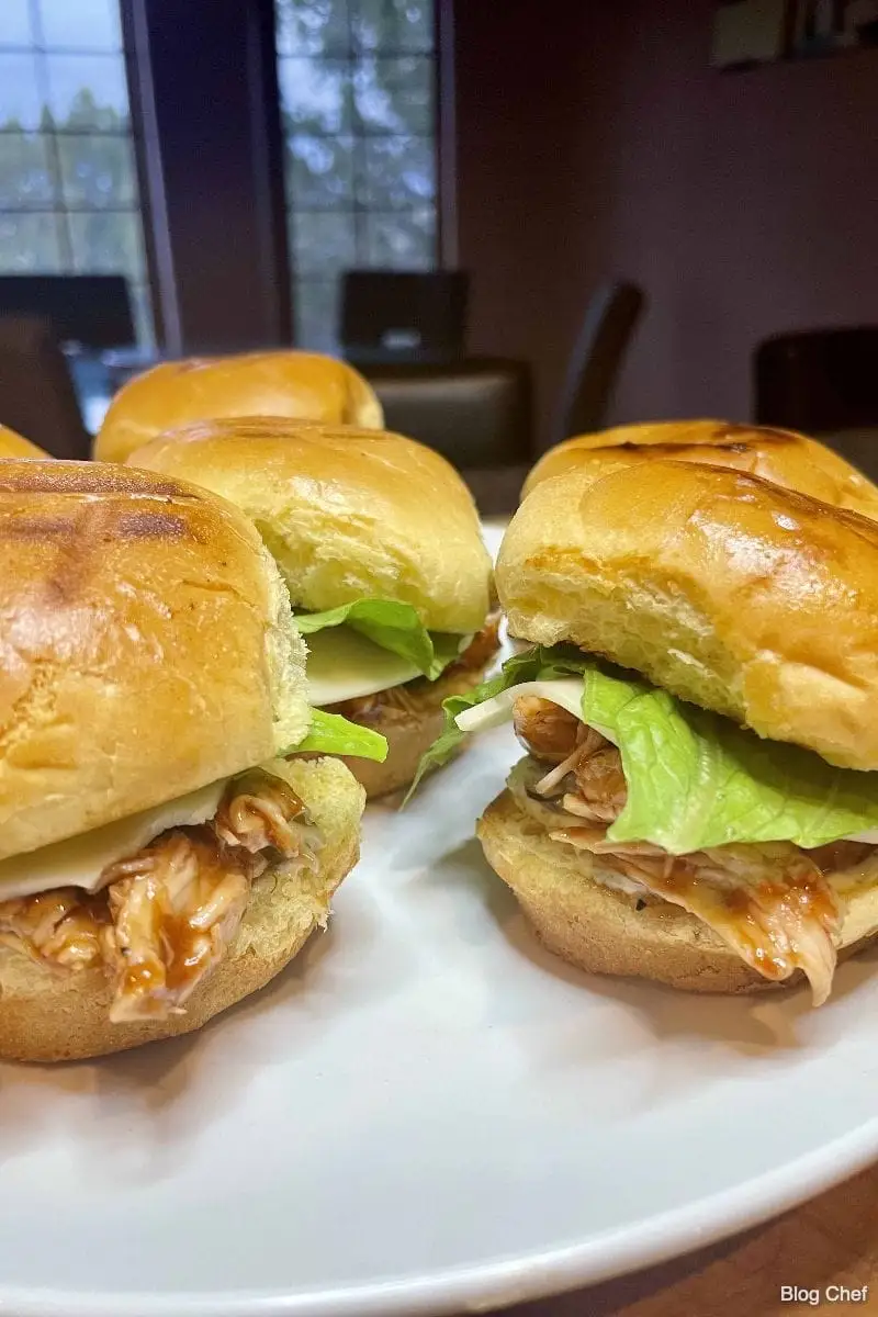 Prepared BBQ chicken sliders on white plate.