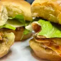 Prepared BBQ chicken sliders on white plate.