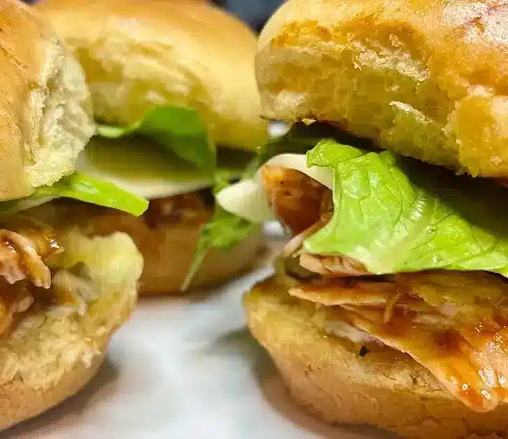 Prepared BBQ chicken sliders on white plate.