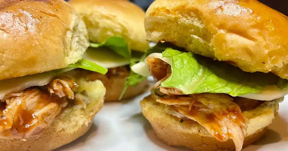 Prepared BBQ chicken sliders on white plate.