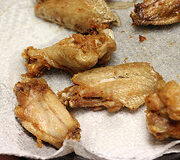 Fried chicken wings resting on a paper towel-lined plate.