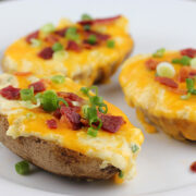 Twice baked potatoes topped with melted cheese, bacon bits, and green onions on a white plate