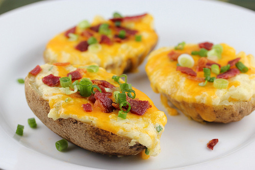 Twice baked potatoes topped with melted cheese, bacon bits, and green onions on a white plate