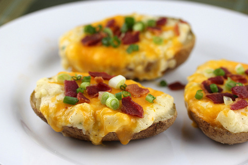 Twice baked potatoes topped with melted cheese, bacon bits, and green onions on a white plate